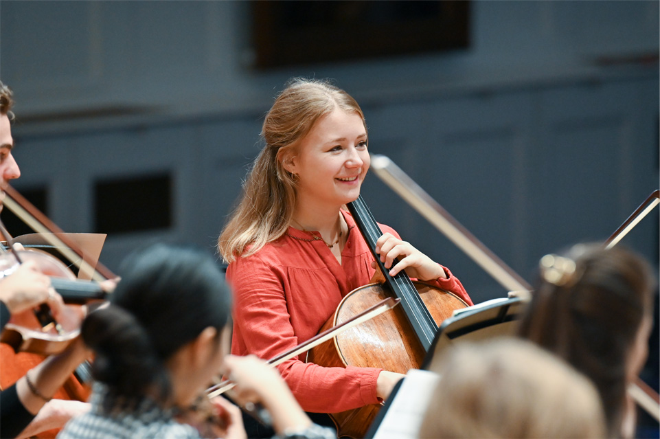 Female student enjoying herself and playing the cello in an orchestra.